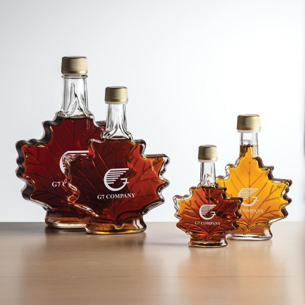 Maple leaf-shaped bottles of maple syrup in various sizes on a wooden surface.